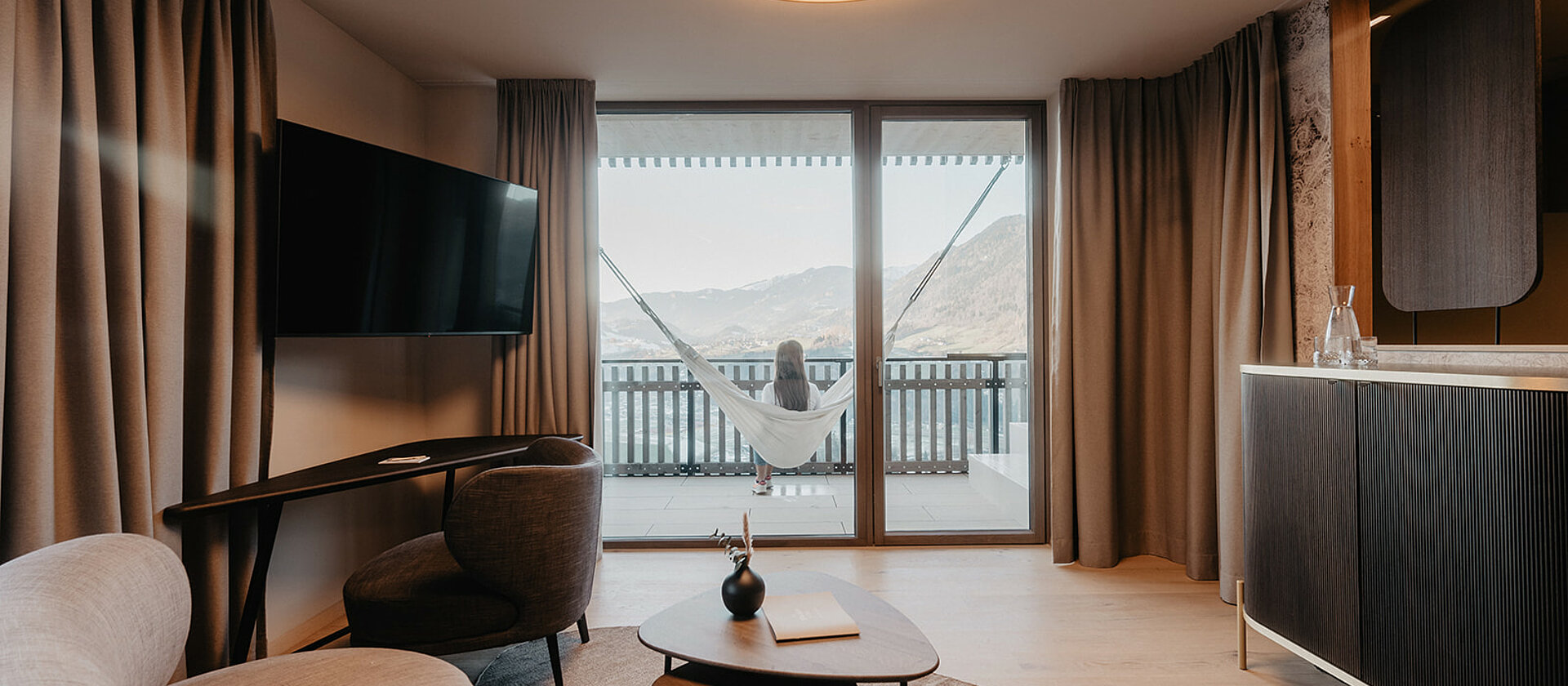 Gemütlicher Wohnbereich der Panorama Suite Premium mit moderner Einrichtung, großer Couch, Schreibtisch und Panoramafenstern im Hotel Berghof in Salzburg.