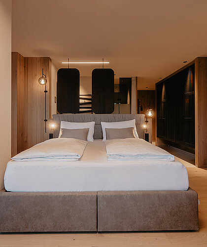 Gemütlicher Schlafbereich einer Suite mit hochwertigem Doppelbett, eleganter Holzverkleidung und modernem Design im Hotel Berghof Salzburg.